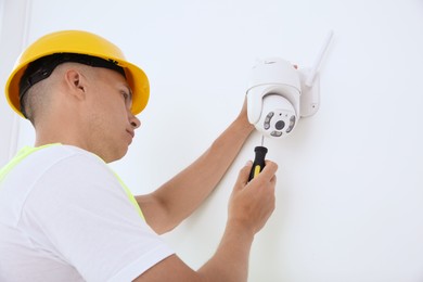 Photo of Technician with screwdriver installing CCTV camera on wall indoors, low angle view