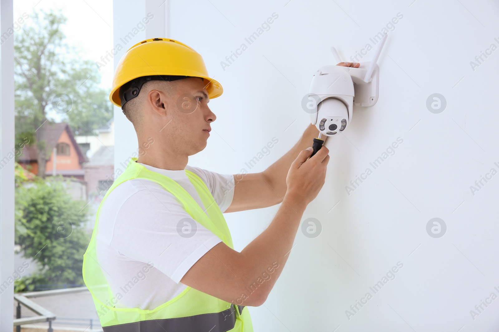 Photo of Technician with screwdriver installing CCTV camera on wall indoors