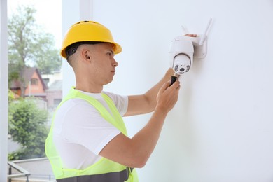 Technician with screwdriver installing CCTV camera on wall indoors