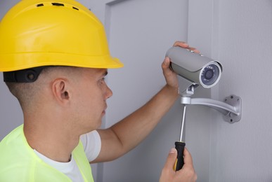 Photo of Technician with screwdriver installing CCTV camera on wall indoors