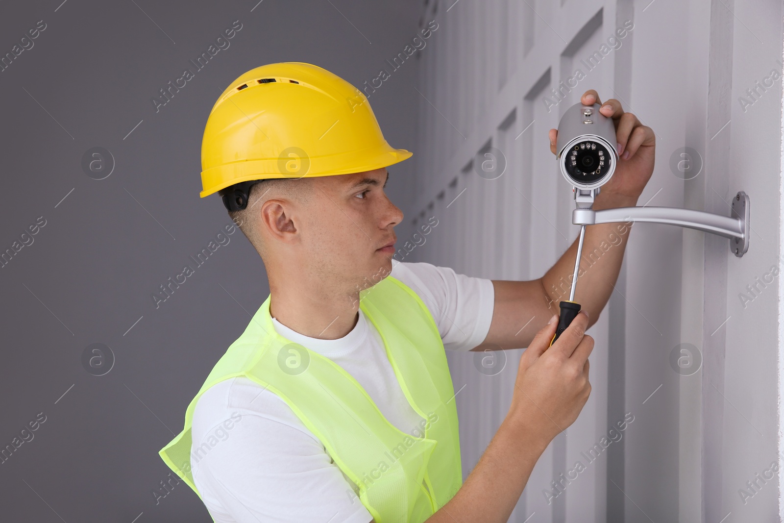 Photo of Technician with screwdriver installing CCTV camera on wall indoors