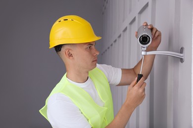 Technician with screwdriver installing CCTV camera on wall indoors