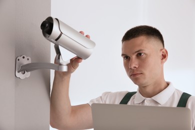 Technician with laptop installing CCTV camera indoors