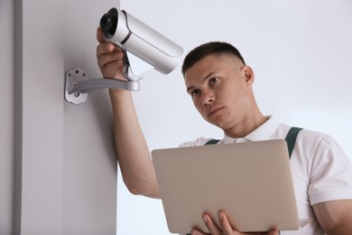 Technician with laptop installing CCTV camera indoors