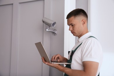 Photo of Technician with laptop installing CCTV camera indoors. Space for text