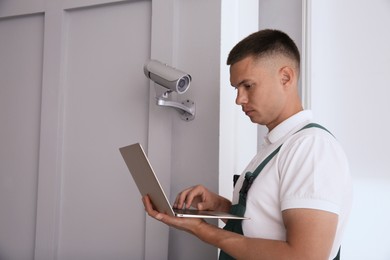 Technician with laptop installing CCTV camera indoors. Space for text