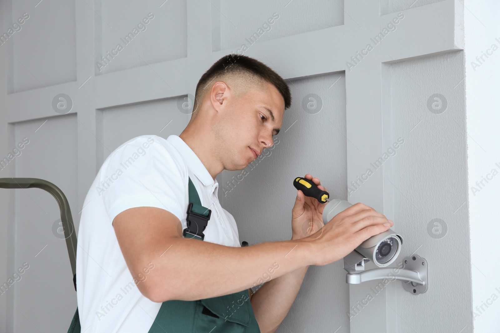 Photo of Technician with screwdriver installing CCTV camera on wall indoors