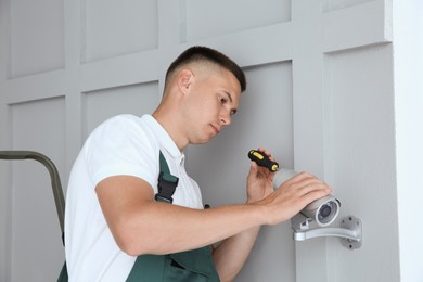 Technician with screwdriver installing CCTV camera on wall indoors