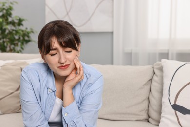 Photo of Upset young woman suffering from toothache at home, space for text