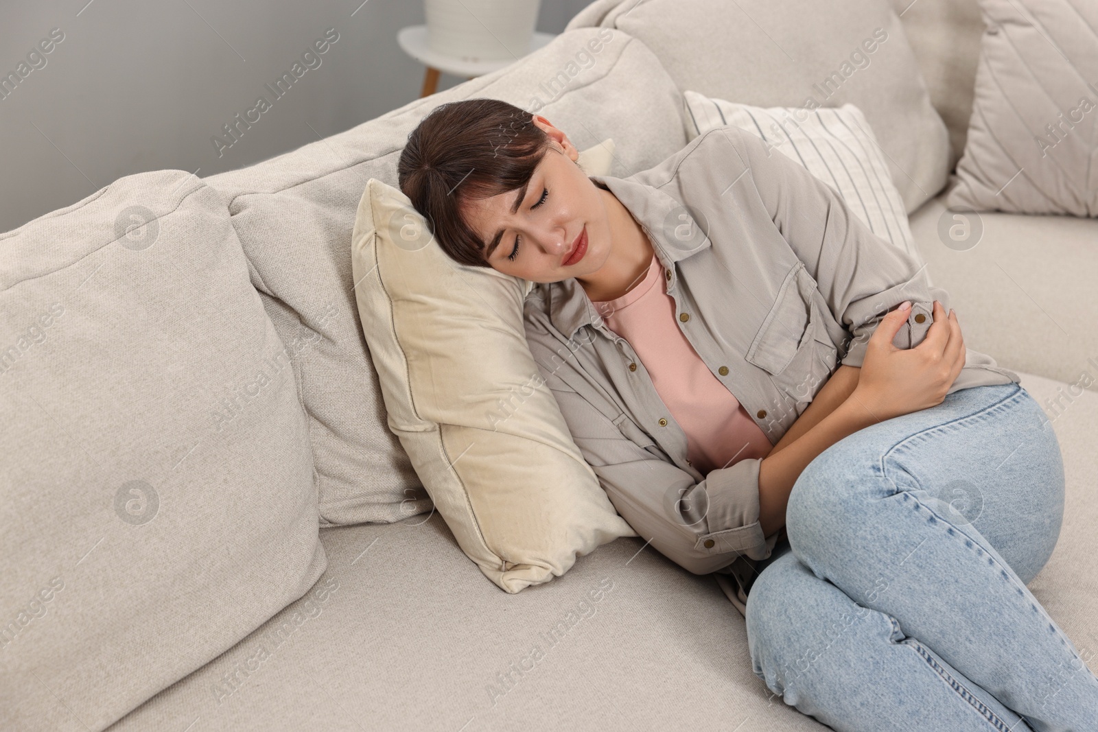 Photo of Upset woman suffering from abdominal pain on sofa at home