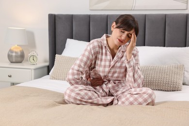Photo of Upset woman suffering from headache on bed at home