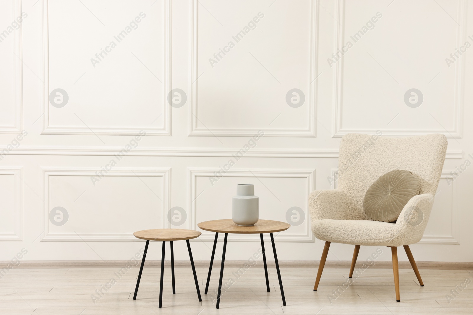 Photo of Soft armchair, coffee tables and lamp in light room