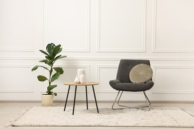 Photo of Soft armchair, coffee table, houseplant and lamp in light room