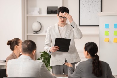 Photo of Man with clipboard feeling embarrassed during business meeting in office