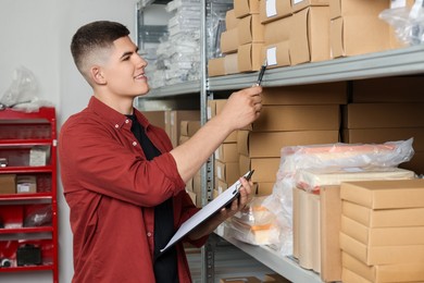 Smiling young man with clipboard near cardboard boxes in auto store