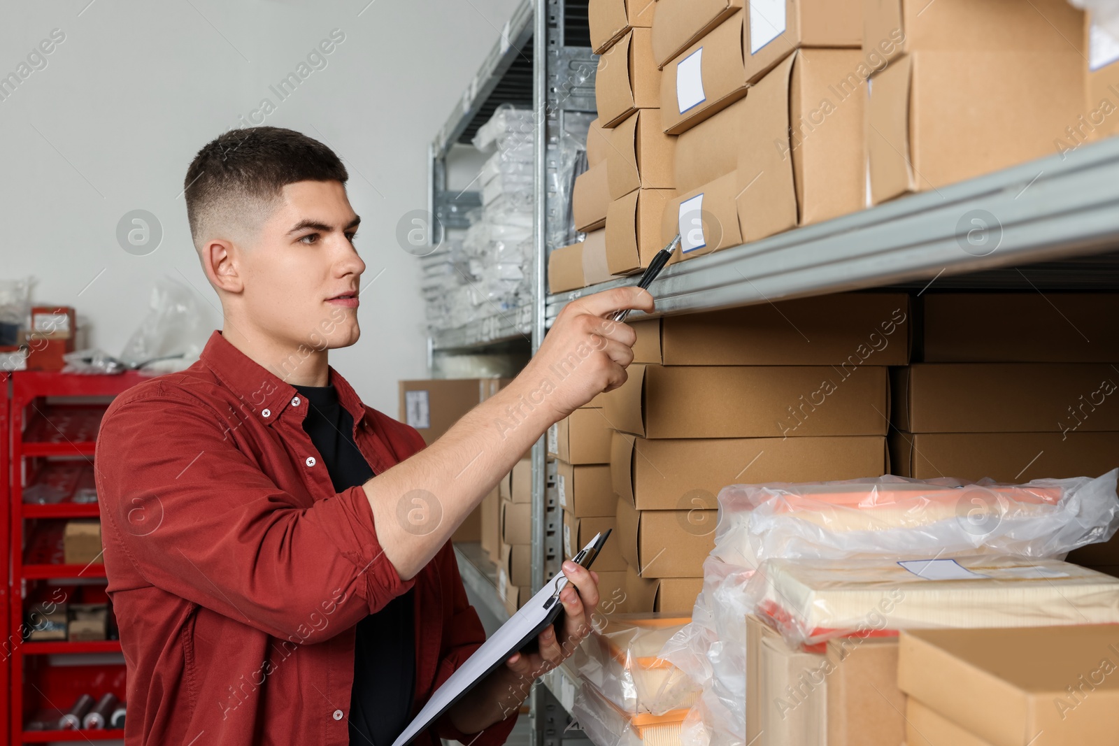 Photo of Young man with pen and clipboard near cardboard boxes in auto store