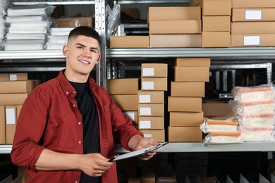 Photo of Smiling young man with clipboard near cardboard boxes in auto store