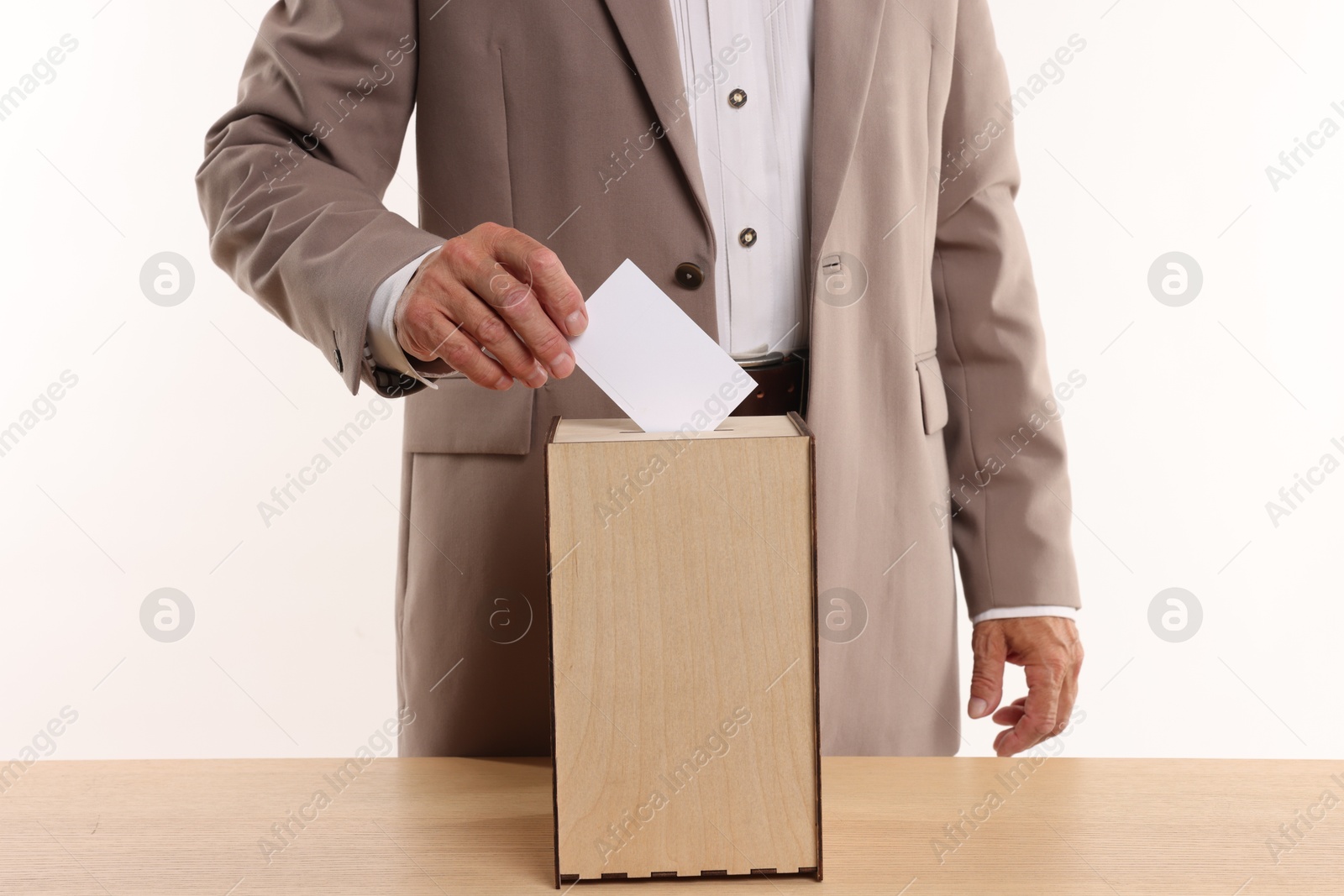 Photo of Referendum. Man putting his vote into ballot box at wooden table against white background, closeup