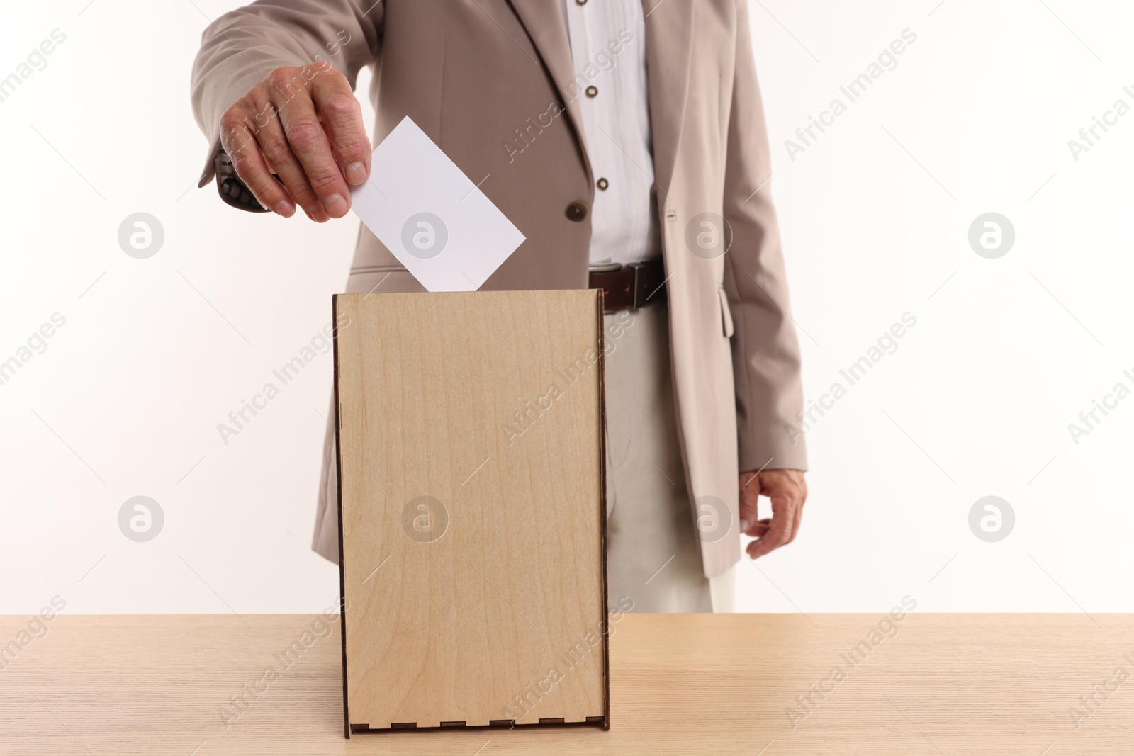 Photo of Referendum. Man putting his vote into ballot box at wooden table against white background, closeup