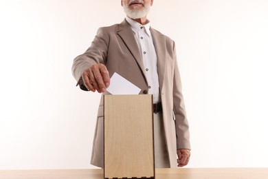 Photo of Referendum. Man putting his vote into ballot box at wooden table against white background, closeup