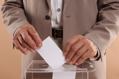 Photo of Referendum. Man putting his vote into ballot box against beige background, closeup