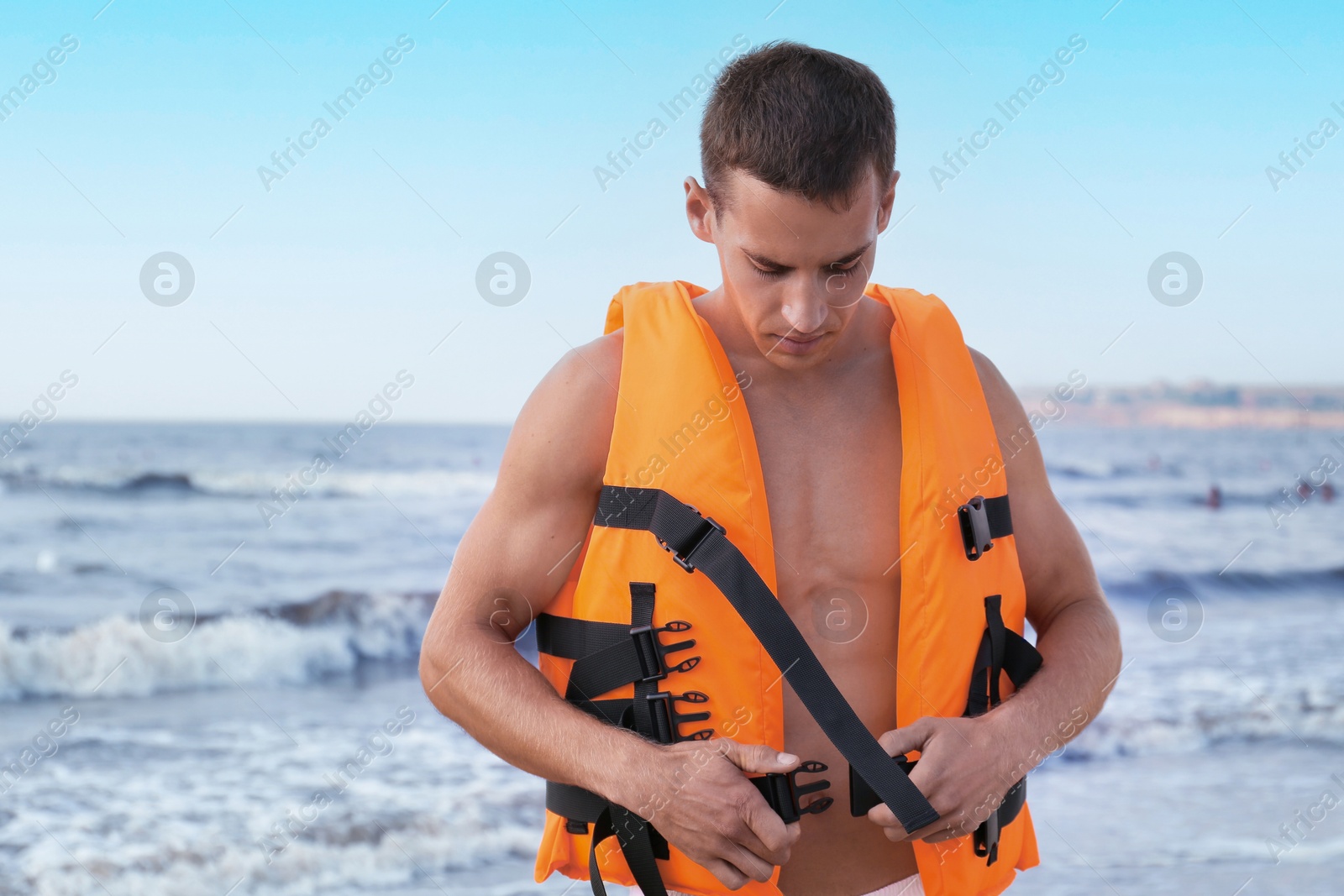 Photo of Handsome lifeguard putting on life vest near sea