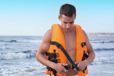 Photo of Handsome lifeguard putting on life vest near sea