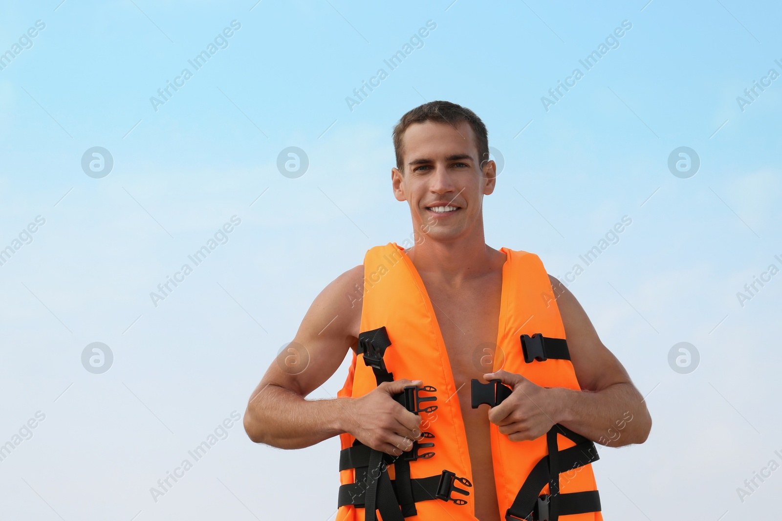 Photo of Handsome lifeguard putting on life vest against sky