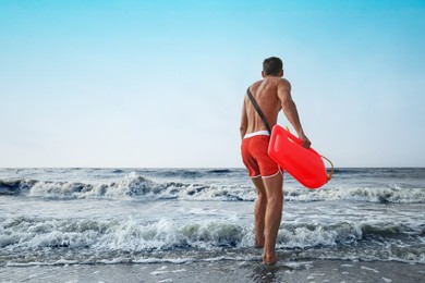 Photo of Handsome lifeguard with life buoy near sea, back view