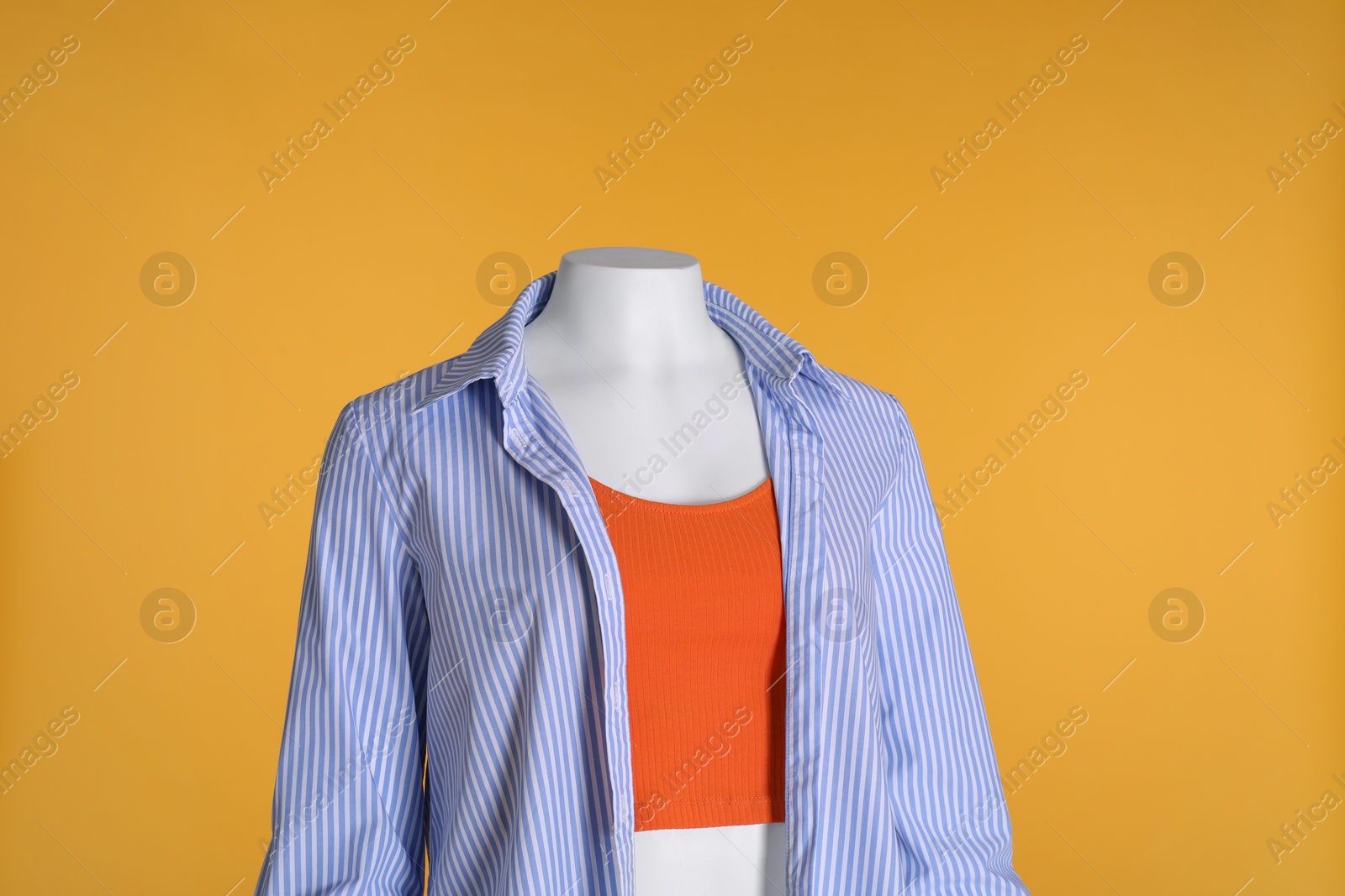 Photo of Female mannequin dressed in stylish tank top and striped shirt on orange background