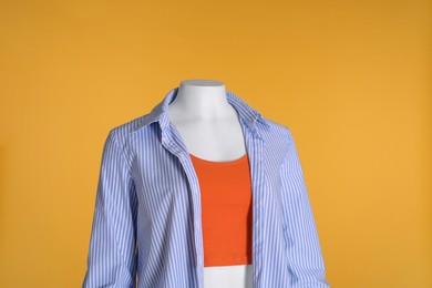 Female mannequin dressed in stylish tank top and striped shirt on orange background