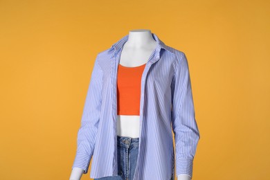 Photo of Female mannequin dressed in tank top, striped shirt and denim shorts on orange background. Stylish outfit
