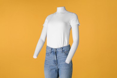 Photo of Female mannequin dressed in white t-shirt and stylish jeans on orange background