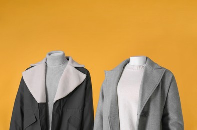 Photo of Mannequins dressed in stylish coat, jacket, sweater and turtleneck on orange background