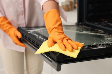 Photo of Woman cleaning oven door with rag in kitchen, closeup