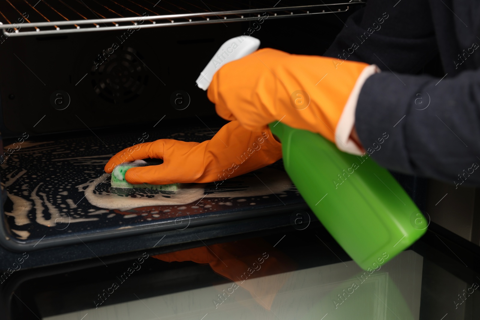 Photo of Woman cleaning oven with sponge and detergent, closeup