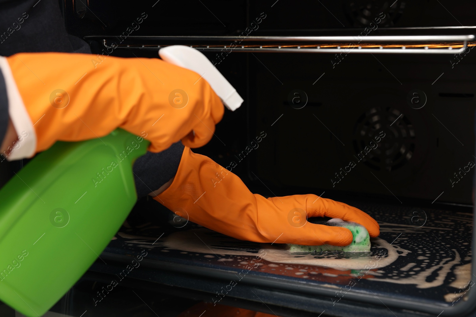 Photo of Woman cleaning oven with sponge and detergent, closeup