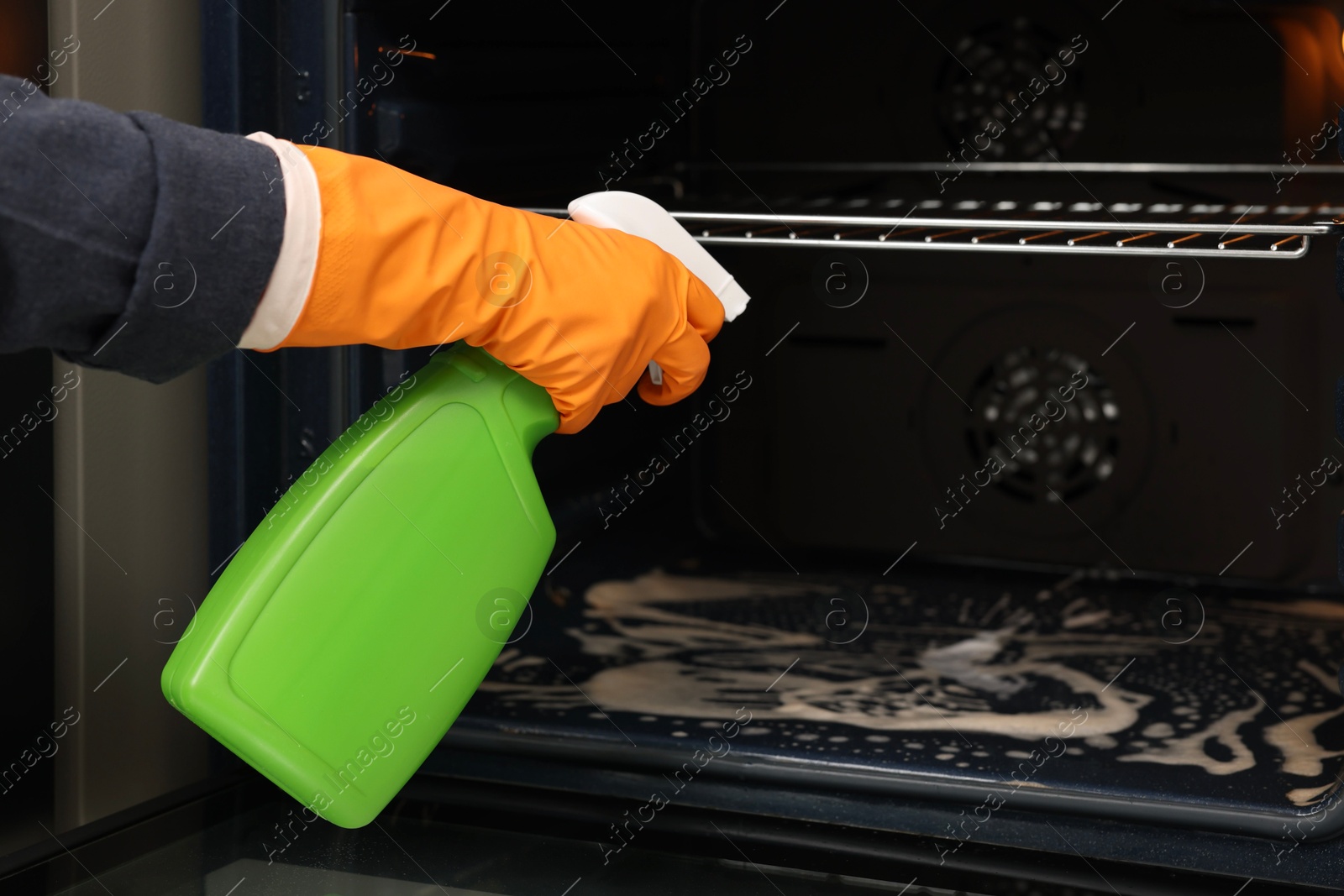 Photo of Woman cleaning oven with detergent, closeup view