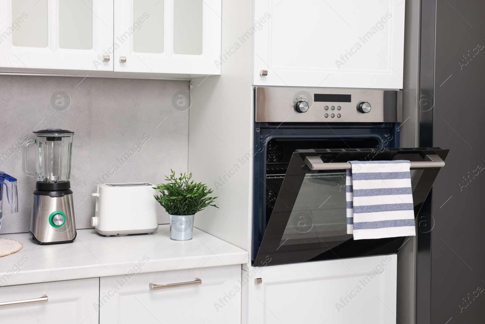 Photo of Open electric oven with striped towel in kitchen. Cooking appliance