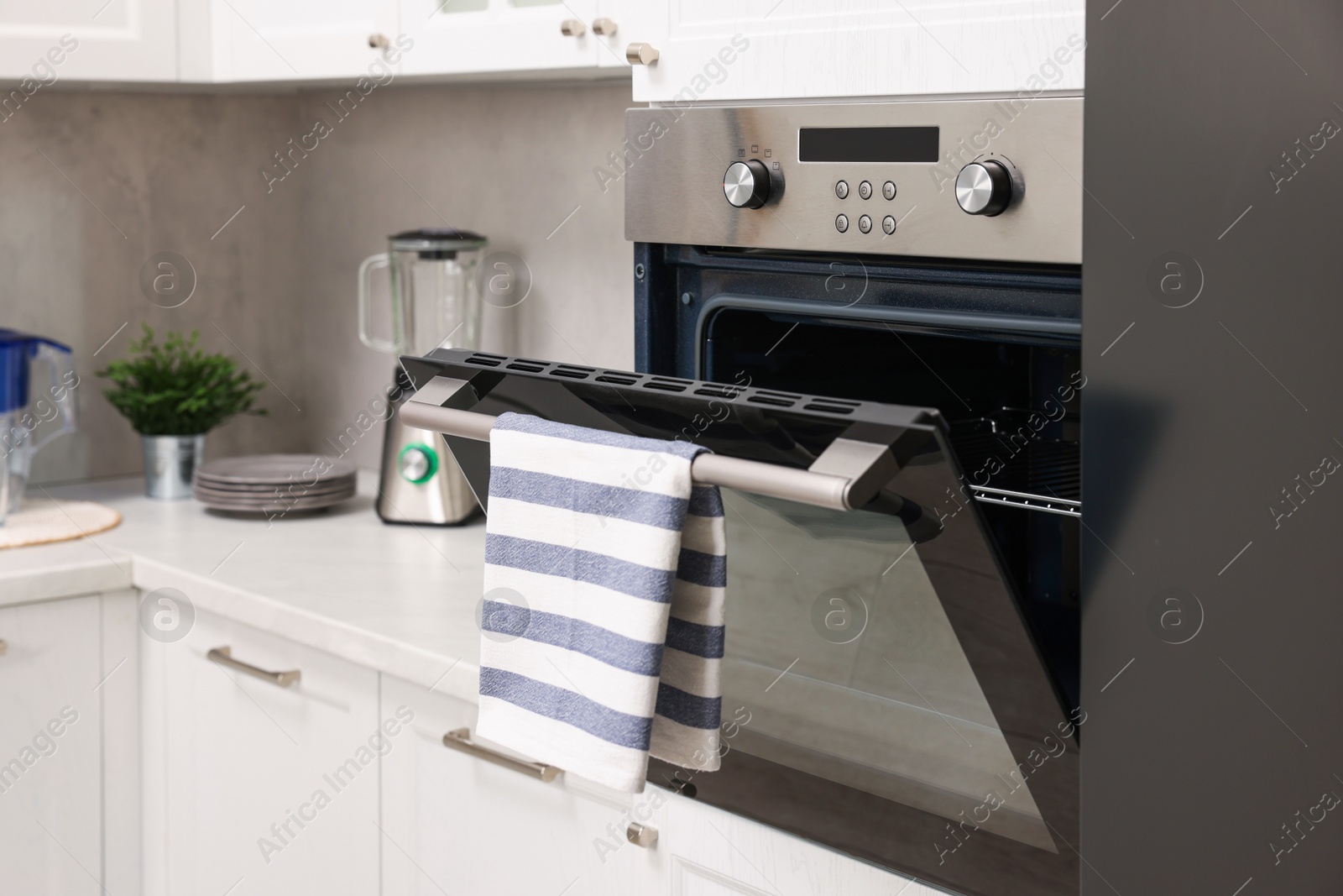 Photo of Open electric oven with striped towel in kitchen. Cooking appliance