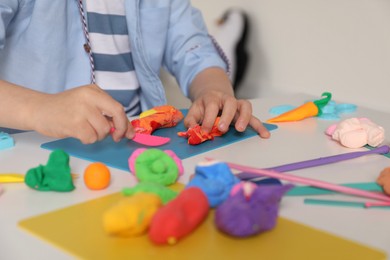 Little boy sculpting with play dough at table indoors, closeup