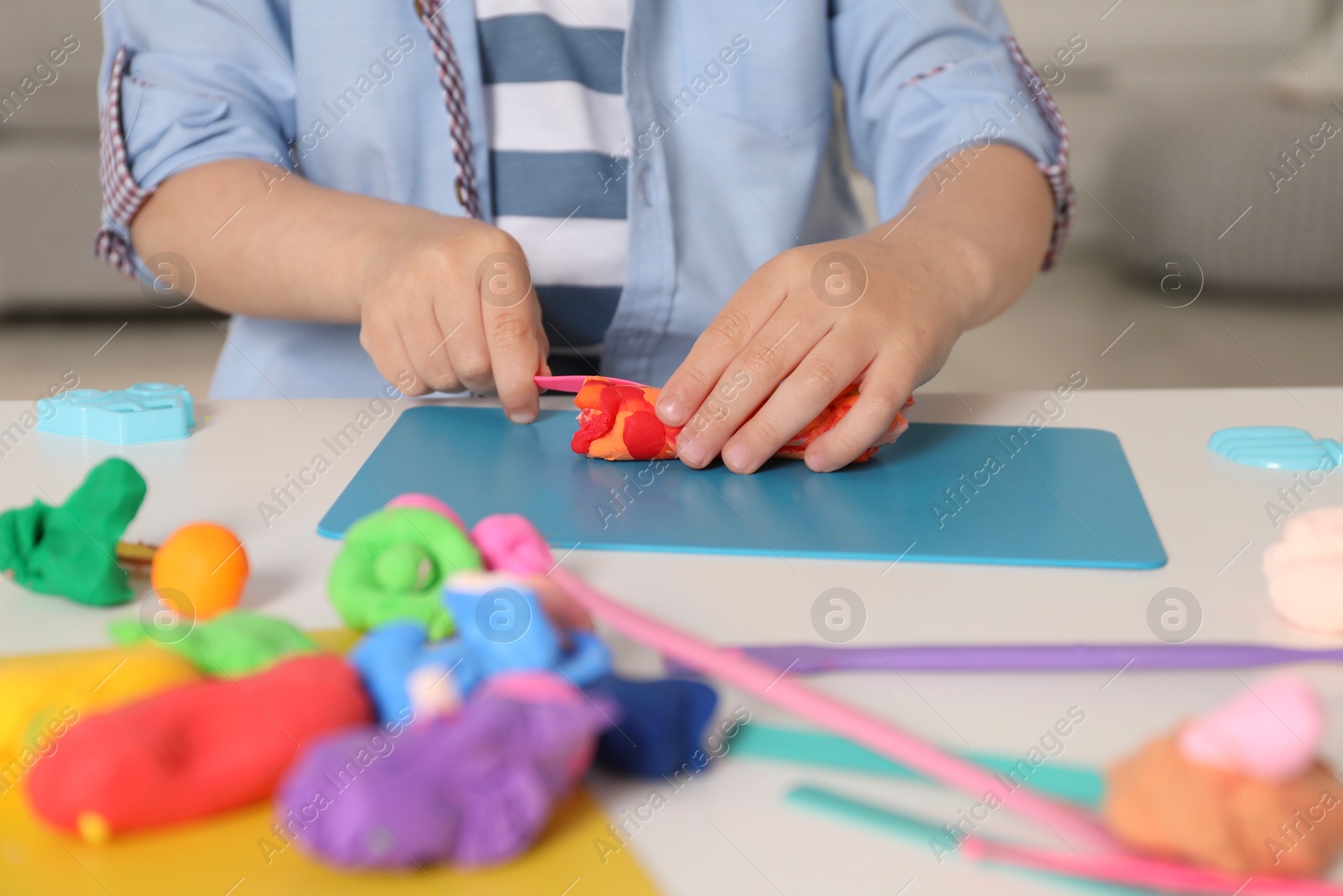 Photo of Little boy sculpting with play dough at table indoors, closeup