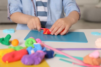 Photo of Little boy sculpting with play dough at table indoors, closeup