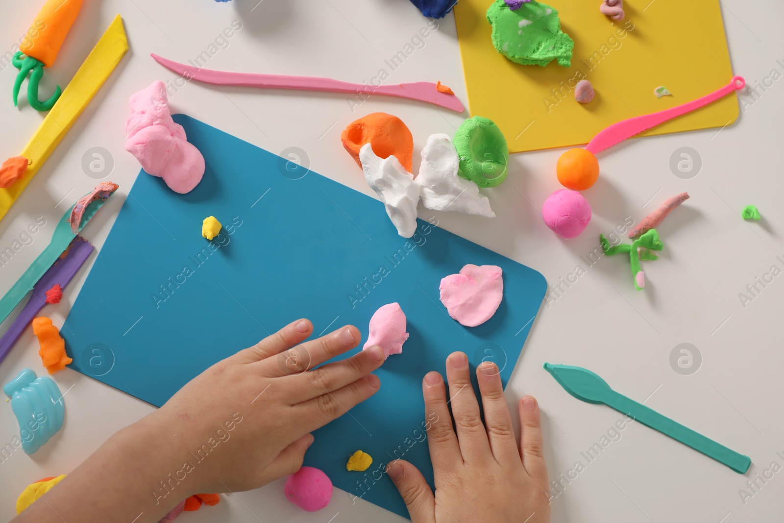 Photo of Boy sculpting with play dough at white table, top view