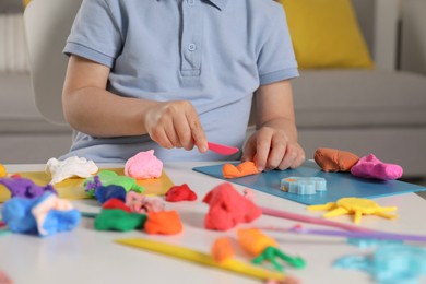 Photo of Little boy sculpting with play dough at table indoors, closeup