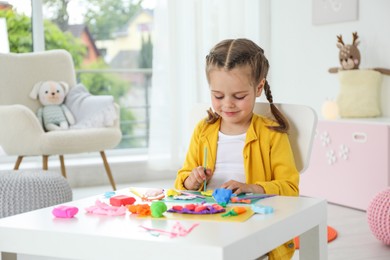 Little girl sculpting with play dough at table in kindergarten