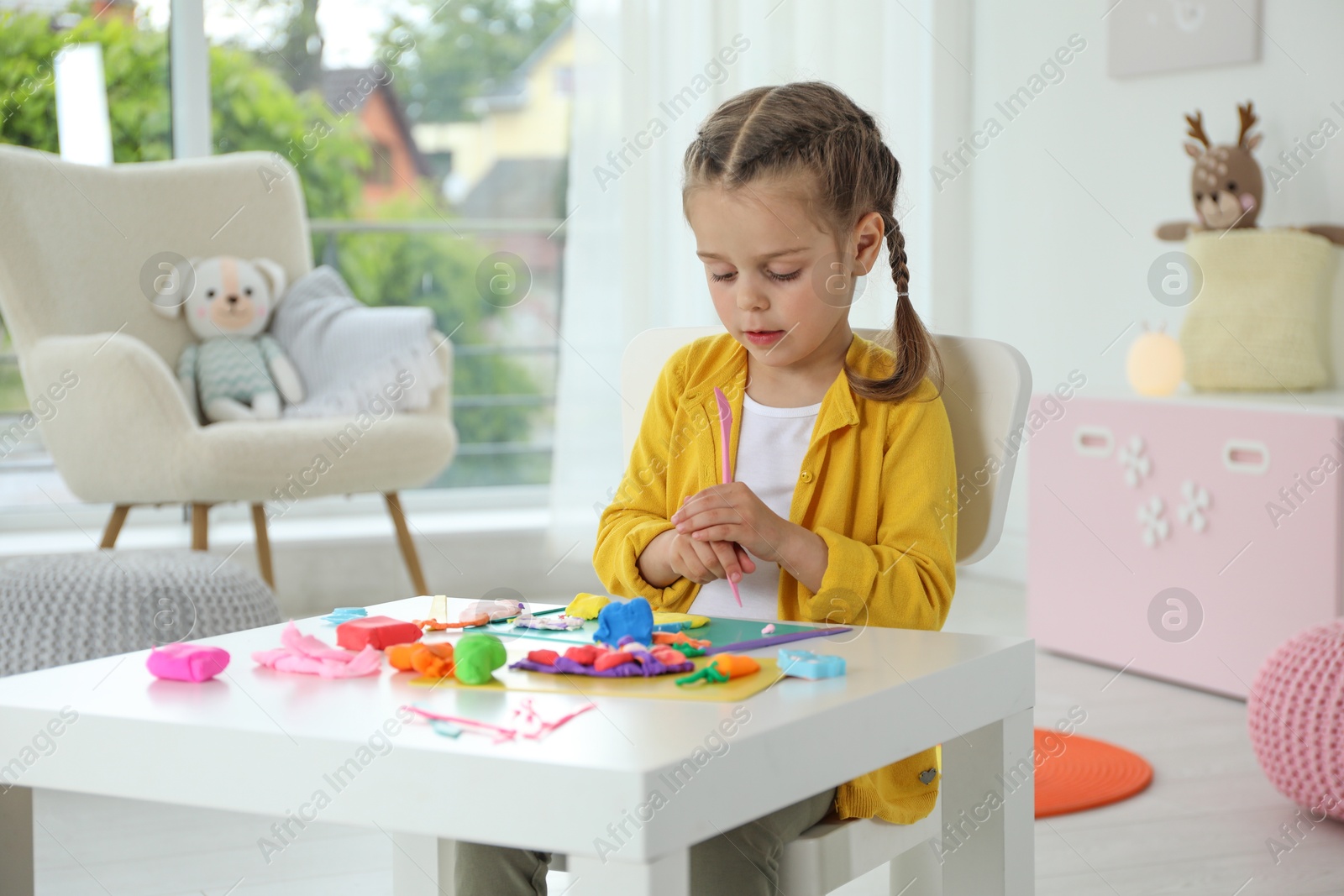 Photo of Little girl sculpting with play dough at table in kindergarten