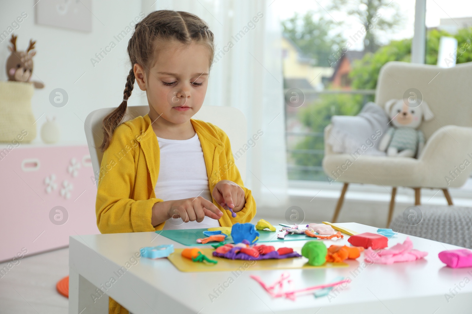 Photo of Little girl sculpting with play dough at table in kindergarten