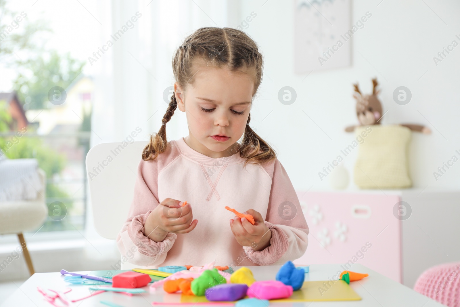 Photo of Little girl sculpting with play dough at table in kindergarten