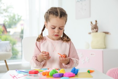 Photo of Little girl sculpting with play dough at table in kindergarten